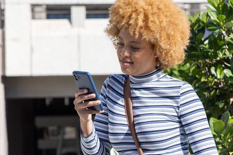 African american woman checking smartphone outdoors on sunny urban campus near building