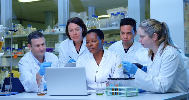 Diverse team of scientists working together in a lab. They are focused on analyzing data on a laptop, surrounded by laboratory equipment.