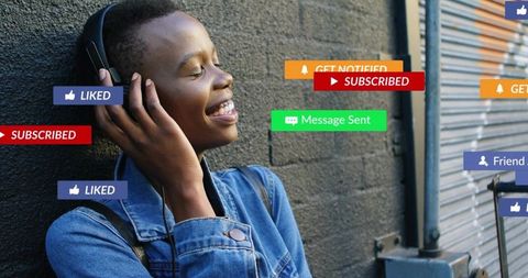 Young Black woman listening to music with headphones on urban wall receiving notifications