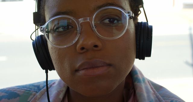 This image shows a close-up of a person wearing headphones and clear glasses. The expression is serious and focused, suggesting involvement or concentration, possibly while studying or enjoying music. Ideal for use in articles or advertisements related to music, concentration, youth culture, eyewear, or lifestyle.