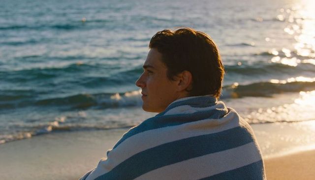 Young man wrapped in striped towel gazing at sunset over calm sea