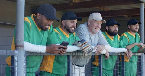 Veteran coach and diverse baseball teammates leaning on dugout rail sharing camaraderie