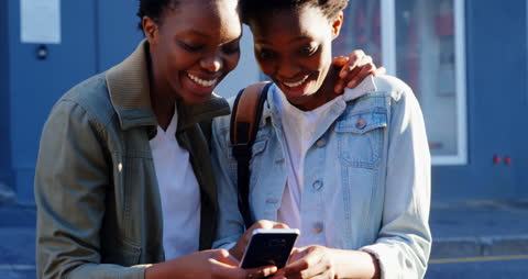 Joyful Twins Sharing Moments on Smartphone in Urban Setting