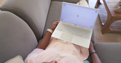 African american man reclining on couch using laptop working remotely at home