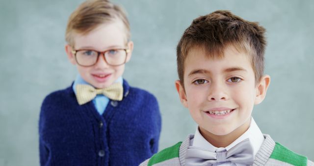 Two Caucasian boys are smiling at the camera, one wearing glasses and a bow tie, the other with a green sweater and bow tie, with copy space. Their cheerful expressions and smart attire suggest a special occasion or a formal event.