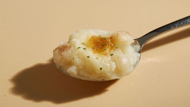 Spoonful of creamy mashed potato with melting butter and parsley garnish on beige surface