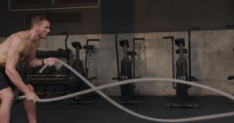 Athletic man training with battle ropes in gym for fitness