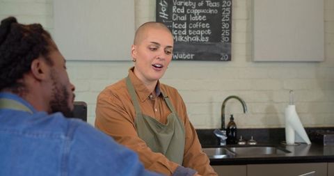 Diverse barista serving customer at modern cafe counter with chalkboard menu
