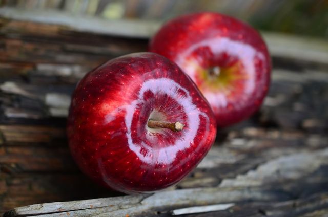 Close-up of two red apples resting on wooden surface. Suitable for advertising healthy eating, nutrition articles, or rustic kitchen decor. Highlight themes of natural foods, freshness, and simplicity. Perfect for use in blogs, magazines, recipe books, and websites promoting health benefits of fruits.