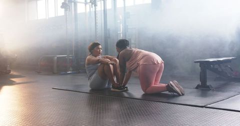 Diverse women training together doing assisted sit-ups on mat in sunlit gym studio