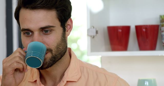 Man drinking coffee in a minimalistic kitchen setting. Ideal for content about morning routines, relaxation, home lifestyle, and kitchen designs.