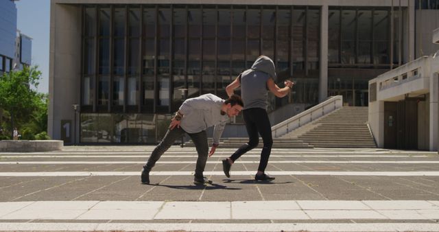 Two dancers are performing a dynamic routine outside a modern building, showcasing their skills in street dance and choreography. The image captures the energy and movement of urban dance against a backdrop of contemporary architecture. This can be used for articles about dance culture, urban arts, or city lifestyles, as well as in promotional materials for dance schools or events.