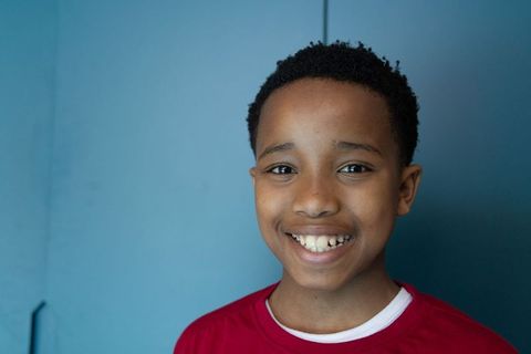 African american boy smiling against blue wall wearing red shirt school portrait