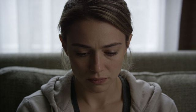 Introspective woman looking downward on sofa with soft window light, closeup portrait