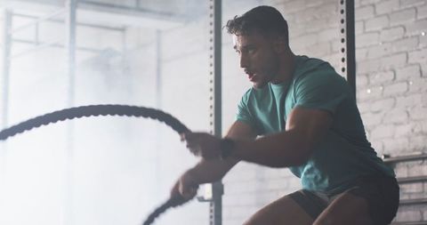 Determined Athlete Training with Battle Ropes in Gym