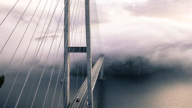 Suspension bridge crossing over serene lake is shrouded in morning mist, highlighting engineering marvel and tranquil natural surroundings. Useful for travel ads, engineering marvel features, scenic calendar images, and nature-related articles.
