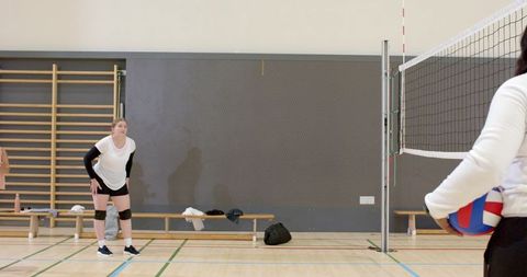 Volleyball teammates practicing ready position on indoor court with net and bench