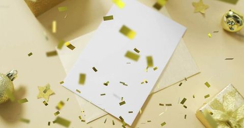Blank greeting card receiving gold confetti over cream envelope with festive gifts