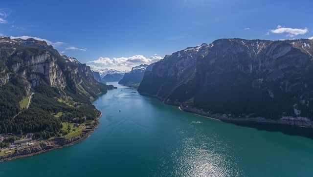 Glinting turquoise alpine lake threading mountain valley with sheer cliffs and village
