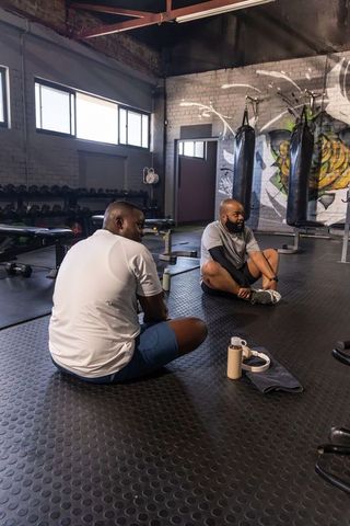 Two african men stretching on gym floor in industrial warehouse fitness training