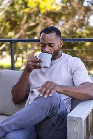 Mature african american man sipping coffee on patio sofa relaxing morning outdoors lifestyle