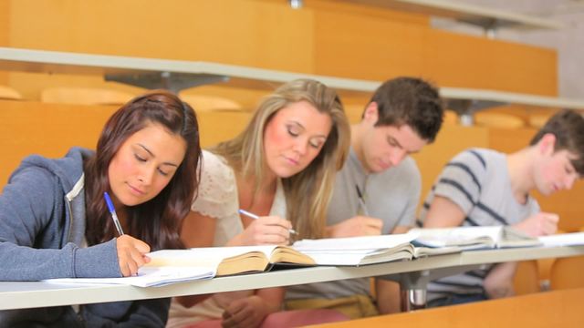 This video shows college students sitting in a lecture hall focusing on writing notes during a class. Ideal for educational websites, school brochures, university promotions, and articles about higher education. It emphasizes group learning, teamwork, and studiousness in an academic setting.