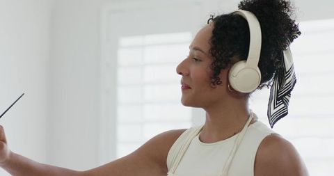 Young woman listening with over-ear headphones tied with patterned scarf in home studio