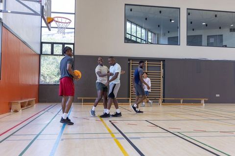 Diverse male friends playing basketball in school gymnasium during daytime pickup game