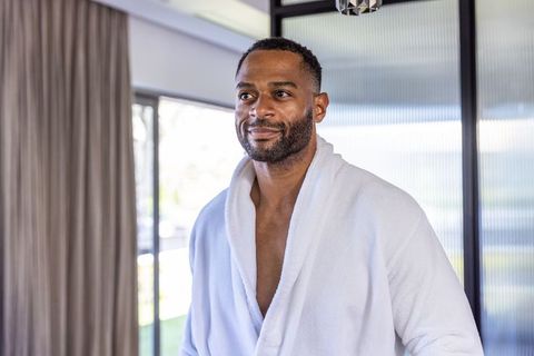 Mature man wearing white robe standing in modern bedroom near frosted glass partition
