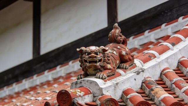 Weathered shisa guardian lion resting on red tile roof ridge with flaked paint and moss