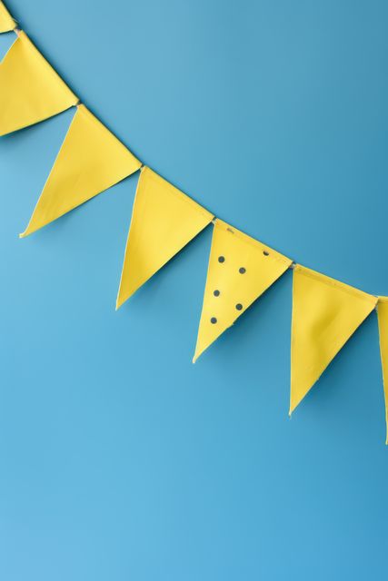 Yellow decorative bunting flags on blue background are ideal for adding a pop of color to parties, events, and celebrations. This image is suitable for designs, advertisements, invitations, banners, and event announcements.