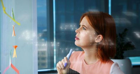 Businesswoman analyzing data on transparent board in modern office