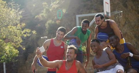 Friends taking selfie after outdoor basketball game on sunny hillside court