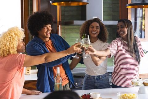 African american friends toasting white wine at kitchen island celebrating friendship