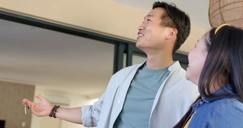 Asian couple touring new apartment holding keys and admiring modern neutral living room