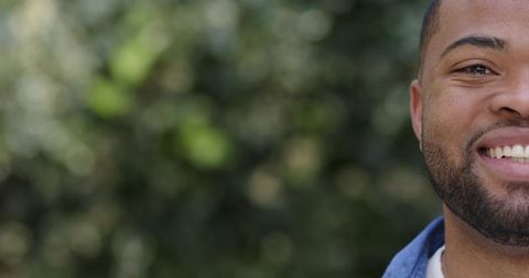 Smiling african american man in denim jacket and white tee outdoors with green bokeh and copy space