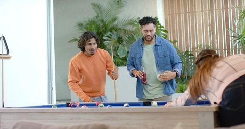 Diverse Friends Playing Pool in Modern Home Lounge Around Blue-Felt Billiards Table