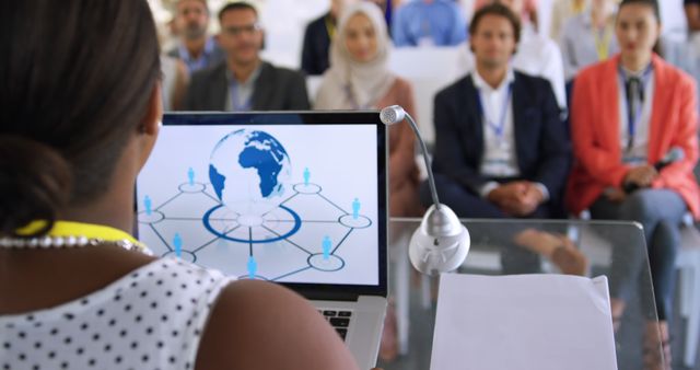 Business professional presenting on global workforce to diverse audience. Ideal for conference presentations, corporate seminars, and business training materials. Highlights use of technology and international networking in business environments.