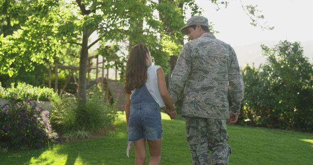 Caucasian male soldier holding hands with daughter in garden, copy space. Soldier, armed forces, home coming, patriotism and defence concept, unaltered.