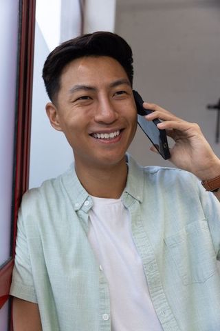 Smiling asian male talking on smartphone indoors by window