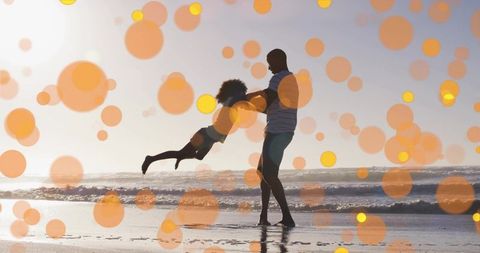 Sunset beach father swinging daughter silhouette with warm orange bokeh and ocean waves