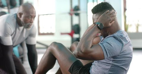 African american trainer coaching client doing crunches wearing smartwatch in gym