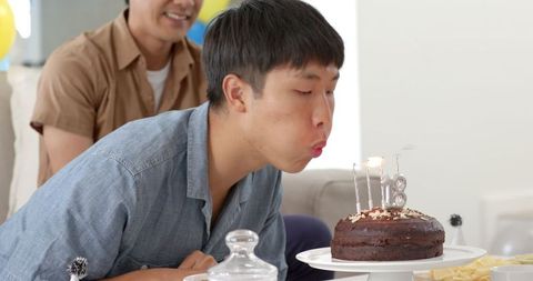 Young Man Blowing Out Birthday Candles on Chocolate Cake