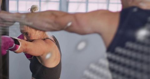 Female boxer sparring with trainer wearing pink gloves in light-filled boxing studio