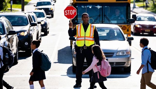 Crossing guard holding stop sign guiding schoolchildren across busy street