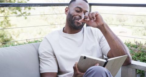Mature man relaxing on balcony writing in journal on sunny terrace for quiet reflection