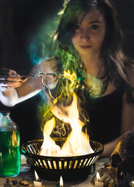 An image of a woman performing a mystical ritual involving burning incense and green flame. She is surrounded by dark ambiance, candles, a potion bottle, and a skull which adds to the occult and spiritual theme. This image can be used for content related to witchcraft, mystical practices, spiritual explorations, or themed storytelling that involves the supernatural and enchantment.