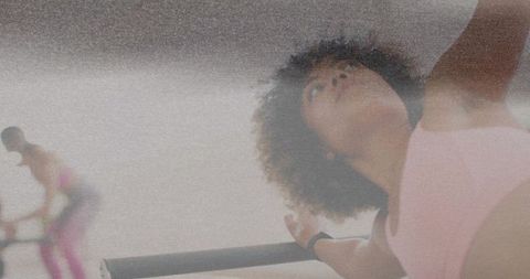 Fit dancer reaching barre during barre workout in pastel gym with grainy film look