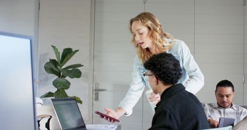 Multicultural team collaborating over laptop and smartphone in modern bright office space with plant
