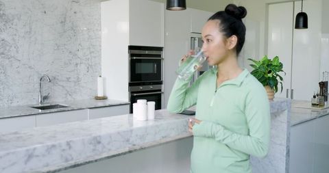 Woman Enjoys Refreshing Water in Modern Marble Kitchen